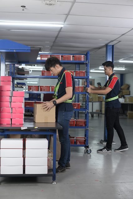 Two colleagues making up orders at the packing benches, finished cartons stacked beside them.